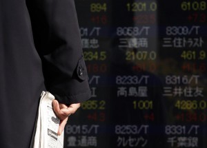A man holding a newspaper looks at an electronic board showing stock prices outside a brokerage in Tokyo