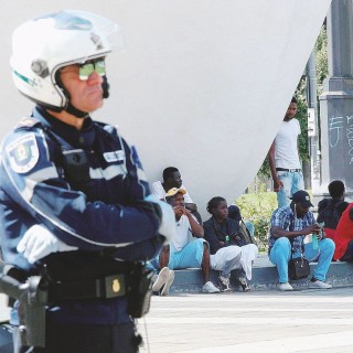 Milano,  agente della polizia urbana  in piazza  Duca d'Aosta  davanti a un gruppo di  migranti  -  Ansa