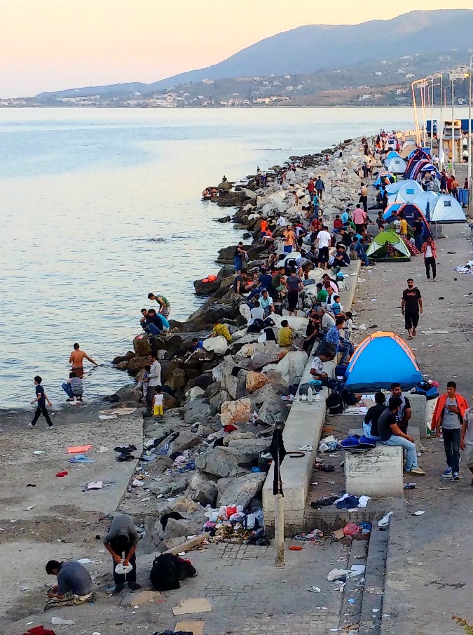 L’esercito silenzioso dei migranti, che sciama per i lungomare e si raduna sul molo: il racconto-reportage dello scrittore Simone Perotti