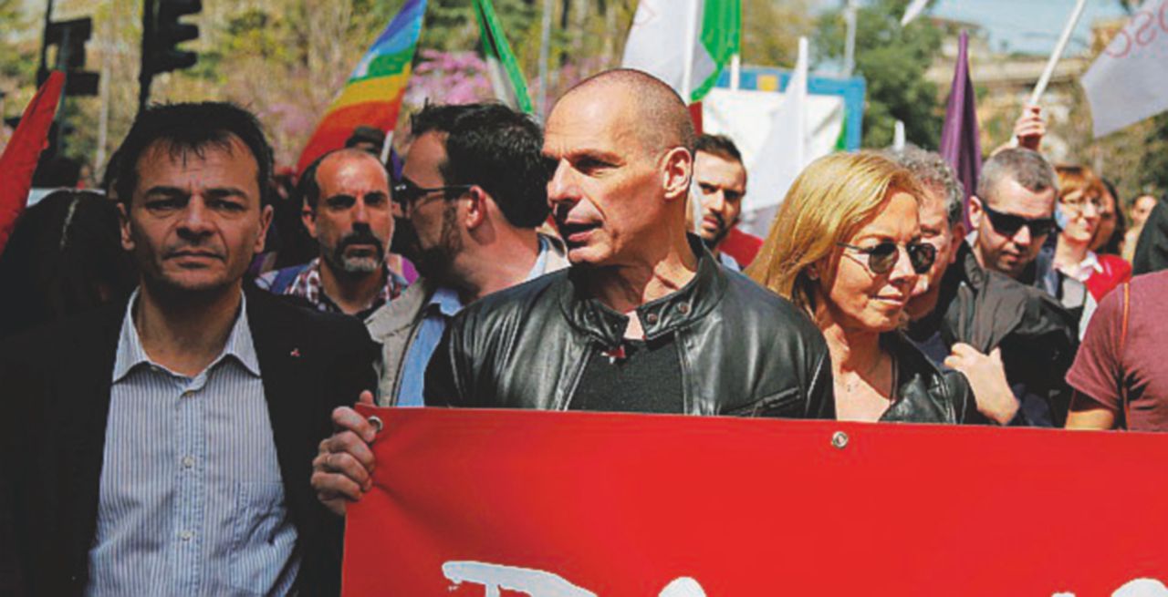 Copertina di Varoufakis procede vicino alle bandiere del “rivale” Tsipras
