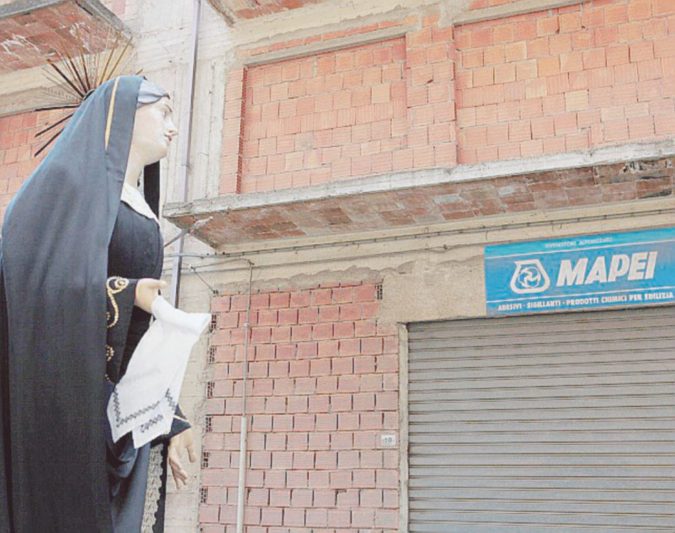A metà - Una processione sfila tra case non finite - Angelo Maggio La capitale del cemento e dell’incompiuto