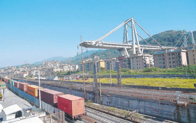 Un treno merci passa vicino a quel che resta di ponte Morandi, a Genova - Ansa Genova, per il ponte tornano in corsa Gavio, l’Anas e Toto