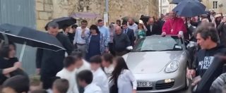 Copertina di Il nuovo arcivescovo festeggia in piedi su una Porsche trainata da 50 bambini: è polemica per l’ambigua processione
