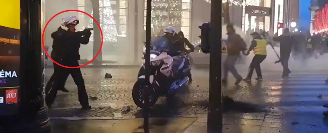 Copertina di Gilet gialli, guerriglia in strada: poliziotto estrae la pistola e la punta contro i manifestanti. Forze dell’ordine in fuga