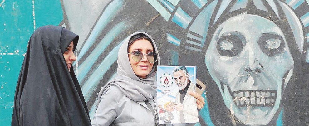 Prove di forza incrociate - Un murales “nero” contro gli Stati Uniti sullo sfondo. In primo piano due donne iraniane, una mostra la foto di Qasem Soleiman, capo delle Guardie della Rivoluzione - Ansa Trump va alla guerra su consiglio di Bolton. Ma la colpa è dei media