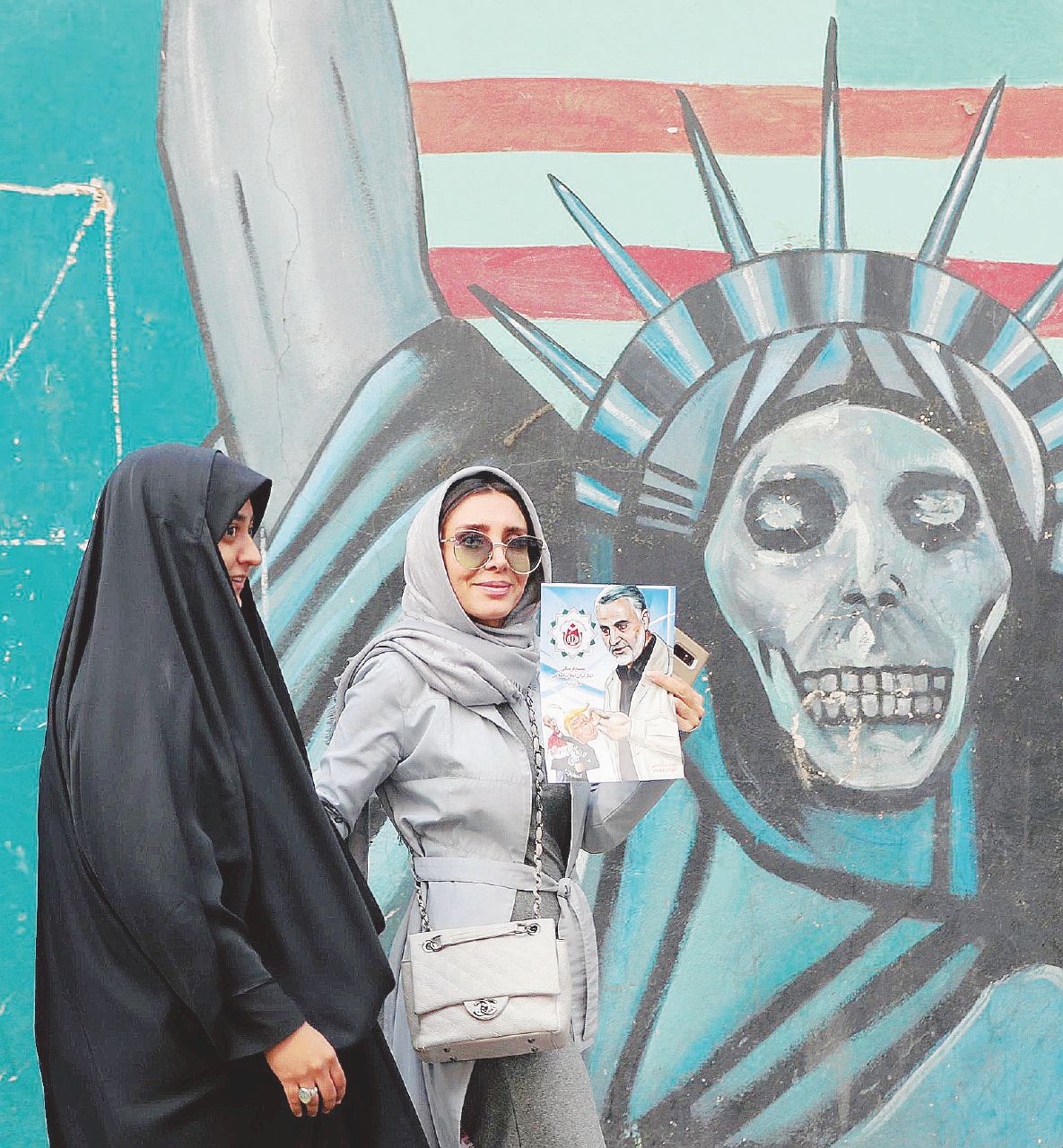 Prove di forza incrociate - Un murales “nero” contro gli Stati Uniti sullo sfondo. In primo piano due donne iraniane, una mostra la foto di Qasem Soleiman, capo delle Guardie della Rivoluzione - Ansa Trump va alla guerra su consiglio di Bolton. Ma la colpa è dei media