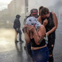 Demonstrators are sprayed water by the police in Santiago, on October 25, 2019, a week after violence protests started. – Demonstrations against a hike in metro ticket prices in Chile’s capital exploded into violence on October 18, unleashing widening protests over living costs and social inequality. (Photo by Martin BERNETTI / AFP)