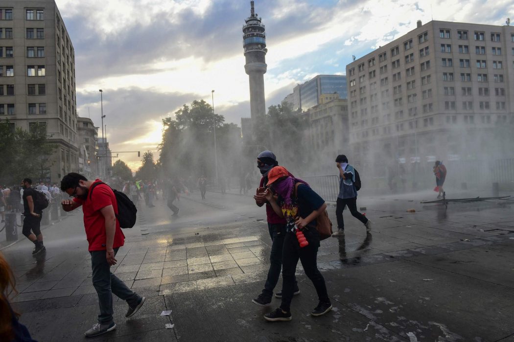 Demonstrators are sprayed water by the police in Santiago, on October 25, 2019, a week after violence protests started. – Demonstrations against a hike in metro ticket prices in Chile’s capital exploded into violence on October 18, unleashing widening protests over living costs and social inequality. (Photo by Martin BERNETTI / AFP)