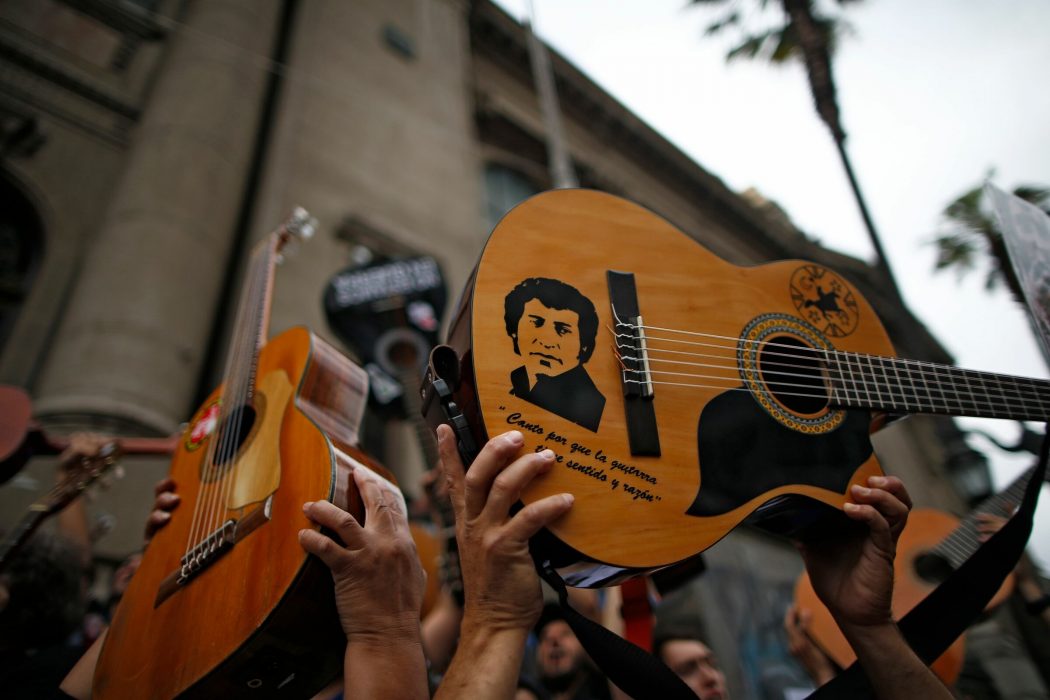 Demonstrators hold up their guitards after performing Chilean musician Victor Jara’s (depicted) "The right to live in peace" in Santiago, on October 25, 2019, a week after violence protests started. – Demonstrations against a hike in metro ticket prices in Chile’s capital exploded into violence on October 18, unleashing widening protests over living costs and social inequality. (Photo by Pablo VERA / AFP)