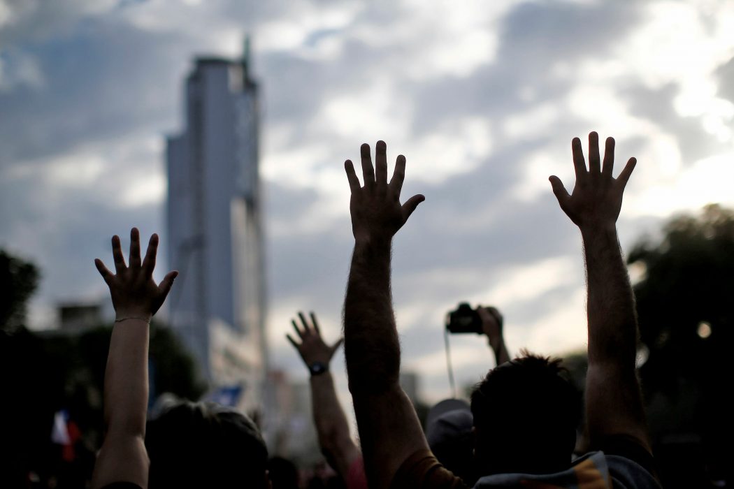 People raise their hands as they demonstrate in Santiago, on October 25, 2019, a week after violence protests started. – Demonstrations against a hike in metro ticket prices in Chile’s capital exploded into violence on October 18, unleashing widening protests over living costs and social inequality. (Photo by Pablo VERA / AFP)