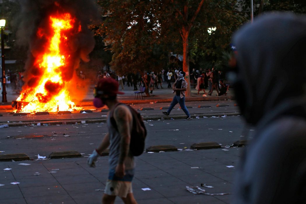 Demonstrators walk near a bonfire in Santiago, on October 25, 2019, a week after violence protests started. – Demonstrations against a hike in metro ticket prices in Chile’s capital exploded into violence on October 18, unleashing widening protests over living costs and social inequality. (Photo by Pablo VERA / AFP)
