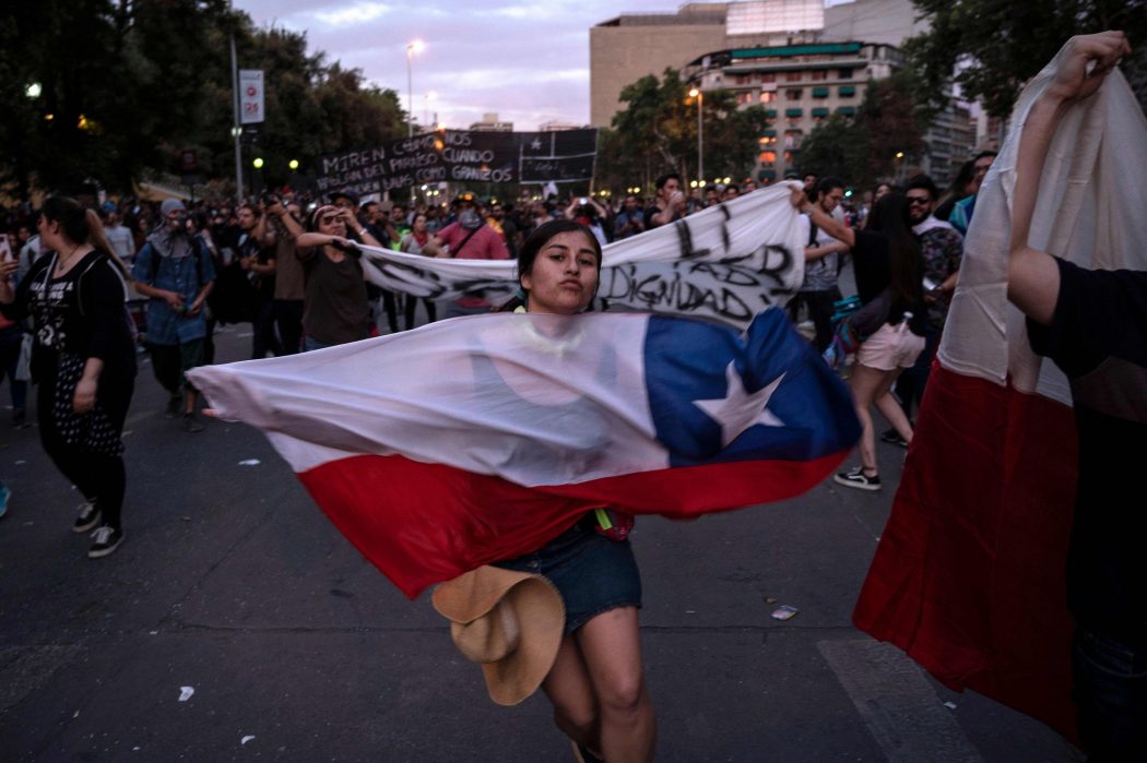 A demonstrator dances with a Chilean national flag in Santiago, on October 25, 2019, a week after protests started. – Demonstrations against a hike in metro ticket prices in Chile’s capital exploded into violence on October 18, unleashing widening protests over living costs and social inequality. (Photo by Pedro Ugarte / AFP)