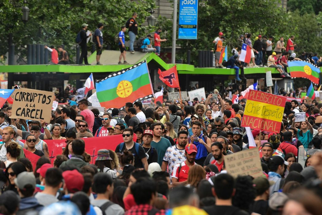 People demonstrate with a Mapuche indigenous flag and signs reading "Corrupts to jail" and "National referendum. Chile woke up" in Santiago, on October 25, 2019, a week after violence protests started. – Demonstrations against a hike in metro ticket prices in Chile’s capital exploded into violence on October 18, unleashing widening protests over living costs and social inequality. (Photo by Martin BERNETTI / AFP)