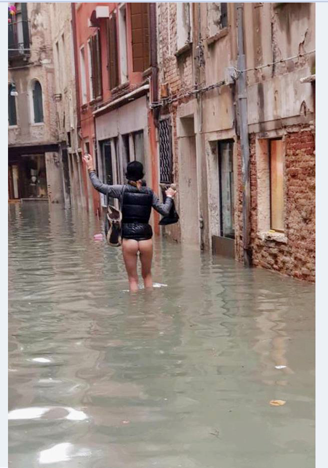 Acqua alta a Venezia, una donna cammina senza vestiti per la calle allagata...