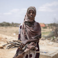 Amina*’s family lived a nomadic pastoralist life before they were displaced and came to the village because of drought. They had a lot of animals (Her mother Anab doesn’t know exactly how many but they used to have goats, sheep and camels) and in a drought in 2018 she lost all but 20 goats and sheep.  

When they first came to the village they couldn’t get food. They are in debt and can’t get credit – they used to get loans from the market to buy food and re-payed them in high season when they took the animals to market. 

Save the Children provided Amina* and Deko*’s mother Anab with a sack of rice, beans, wheat flour, cooking oil and milk at the beginning of July. Before, they were only able to have two meals per day. Now, since Save the Children has helped them, they have three meals a day. She says this is important as if you get weak here, other things can happen to you.

Anab says that daily life in the village is different to that in the countryside. Getting water is very expensive and to transport it you have to rent a car. Before she would use the camels to transport the water. Also there are no health facilities here, so if a child gets sick they have to go to the nearest town of Gardo. Also there are no toilets. 

She hopes for a better future and to build a school and health facilities here. Her children don’t currently go to school but they go to the madrasa since they lived here.

Anab gets sad when she sees her children sick and she doesn’t have the ability to send them to hospital. Her husband (not photographed) is currently sick and she is not able to take him to hospital. 

The family are trying to fatten up their remaining goats to take to market, but apart from that they have no other source of income.