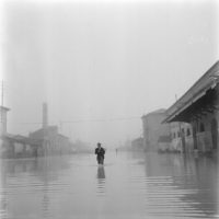 Un fotoreporter con la sua macchina fotografica cammina nell’acqua durante l’alluvione nelle campagne del Polesine_ 17 novembre 1951 ©Archivio Publifoto Intesa Sanpaolo