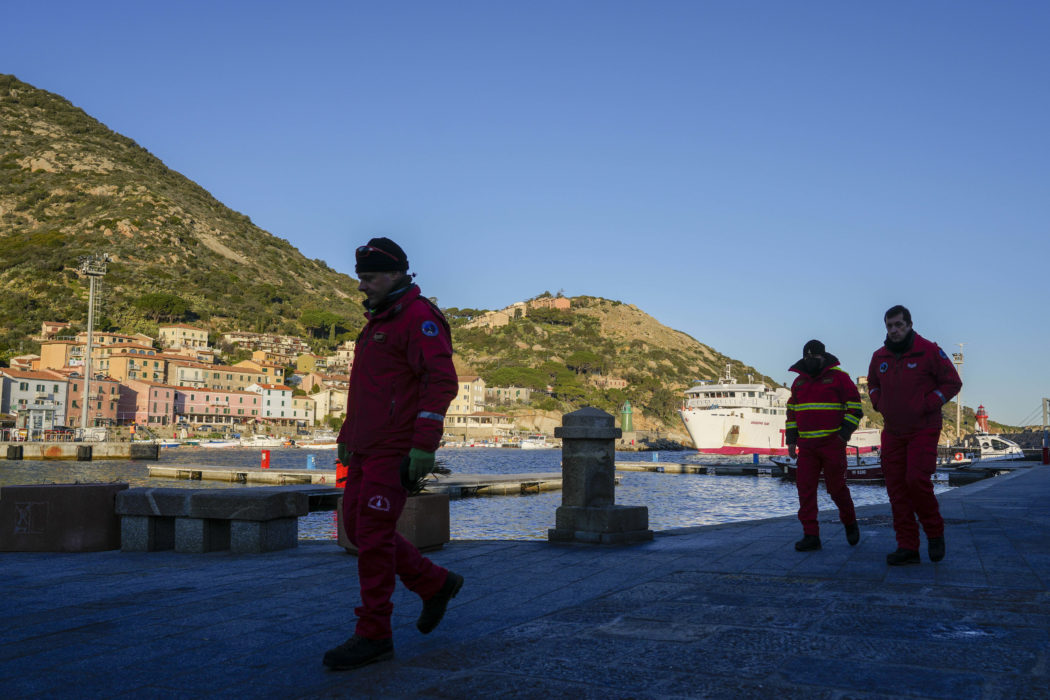 Firefighters walk on a pier of the port of the tiny Tuscan island of Isola del Giglio, Italy, as a ferry boat enters it, Thursday, Jan. 13, 2022. Italy on Thursday is marking the 10th anniversary of the Costa Concordia cruise ship disaster with a daylong commemoration, honoring the 32 people who died but also the extraordinary response by the residents of Giglio who took in the 4,200 passengers and crew from the ship on that rainy Friday night and then lived with the Concordia carcass for another two years before it was hauled away for scrap. (AP Photo/Andrew Medichini)