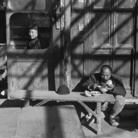 Un cameriere siede alla finestra aperta di una taverna, mentre un “coolie” mangia all’esterno sotto una pergola. Pechino, dicembre 1948. Gelatin silver print, 1957 © Fondation Henri Cartier-Bresson / Magnum Photos 