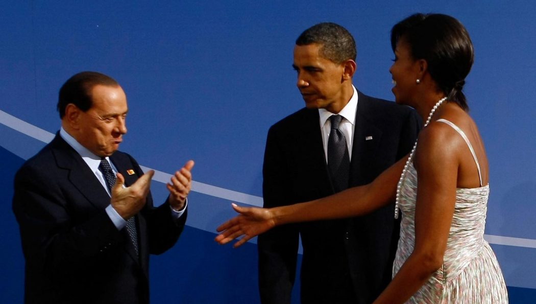 Una delle gaffe storiche: all’arrivo di Obama con la moglie Michelle, l’ex premier si lascia andare a un gesto eloquente di apprezzamento e Obama lo fulmina con lo sguardo
