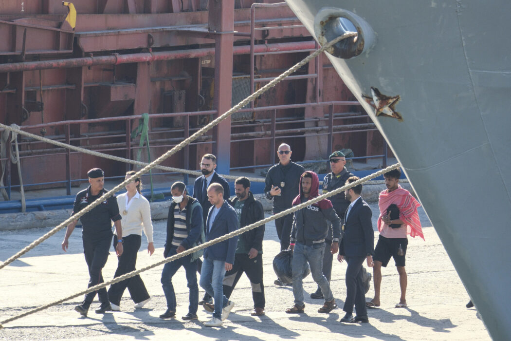 Migrantw and security officials walk at the port of Shengjin, northwestern Albania. Wednesday, Oct. 16, 2024 after disembarking from the Italian navy ship Libra, carrying the first group of 16 migrants intercepted in international waters. (AP Photo/Vlasov Sulaj)