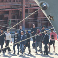 Migrantw and security officials walk at the port of Shengjin, northwestern Albania. Wednesday, Oct. 16, 2024 after disembarking from the Italian navy ship Libra, carrying the first group of 16 migrants intercepted in international waters. (AP Photo/Vlasov Sulaj)