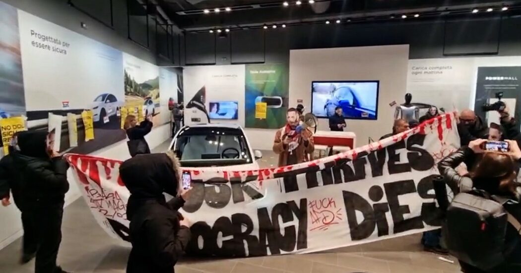 Blitz in una concessionaria Tesla di Milano, attivisti entrano con le maschere di Musk: “Lui prospera, la democrazia muore”