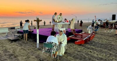 Copertina di Siamo stati alla messa in spiaggia all’alba di Ferragosto a Rimini: qui Dio si prega in infradito, le confessioni si fanno sui lettini. E arriva il ‘TripAdvisor’ delle chiese