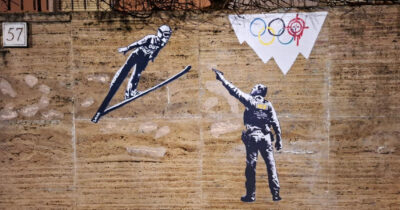 Copertina di Un agente dell’ICE che punta la pistola a uno ski jumper: il nuovo murales di Laika davanti alla sede del CONI a Roma