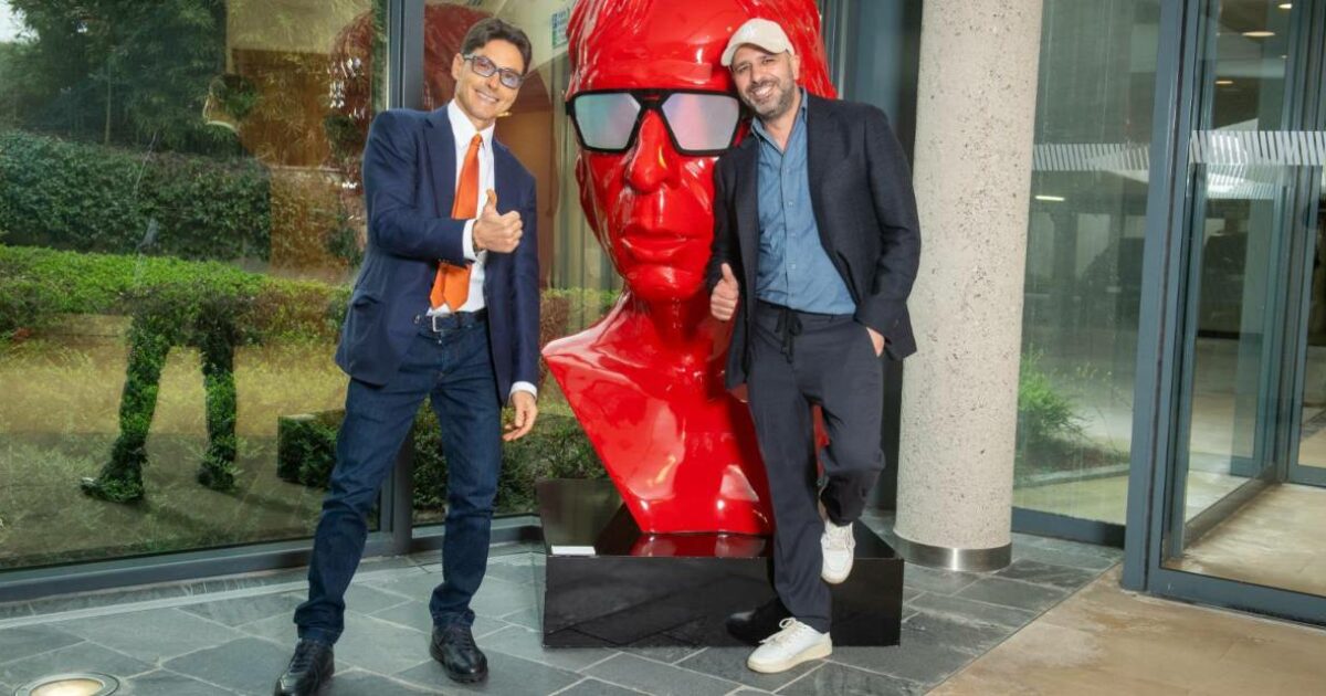 Checco Zalone e Pier Silvio Berlusconi, a sorpresa, si danno il cinque a Cologno Monzese: a “benedirli” l’enorme statua rossa con la faccia dell’attore
