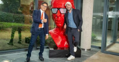 Copertina di Checco Zalone e Pier Silvio Berlusconi, a sorpresa, si danno il cinque a Cologno Monzese: a “benedirli” l’enorme statua rossa con la faccia dell’attore