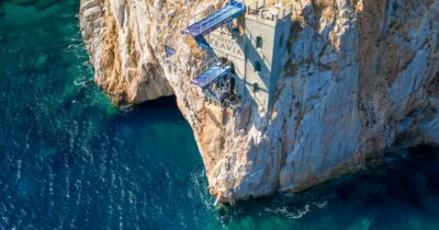 Copertina di Il celebre “Salto della Fede” da 27 metri: lo spettacolo dei tuffi a Porto Flavia e il tributo ad Assassin’s Creed