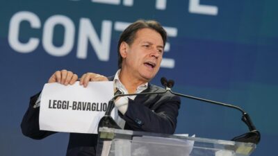 Copertina di Conte strappa le leggi del governo Meloni sul palco di Nova: “Faremo tabula rasa di riarmo, accordi con Israele e salvaladri”