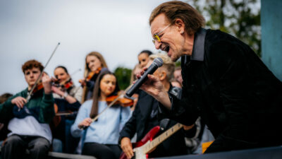 Copertina di “Se il mondo è avvolto dall’oscurità, noi non dobbiamo esserlo”: gli U2 tornano a scuola 50 anni dopo il primo concerto nel cortile del Mount Temple di Dublino – VIDEO